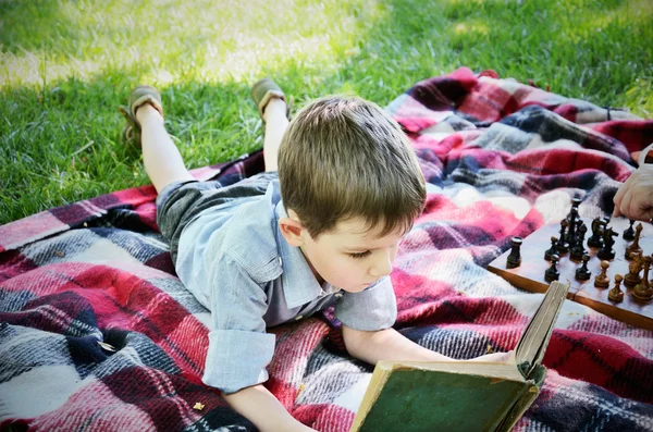 Kleiner Junge liest ein Buch, während er im Park auf einer Matte liegt — Stockfoto