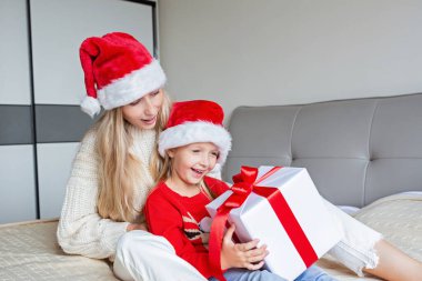 Mutlu Noeller ve mutlu yıllar. Mutlu bir anne ve yatakta tatlı bir kız çocuğu. Ebeveynler ve küçük çocuklar Coronavirus covid-19 karantinası sırasında evde eğleniyorlar. Odasında hediyeler olan sevgi dolu bir aile.