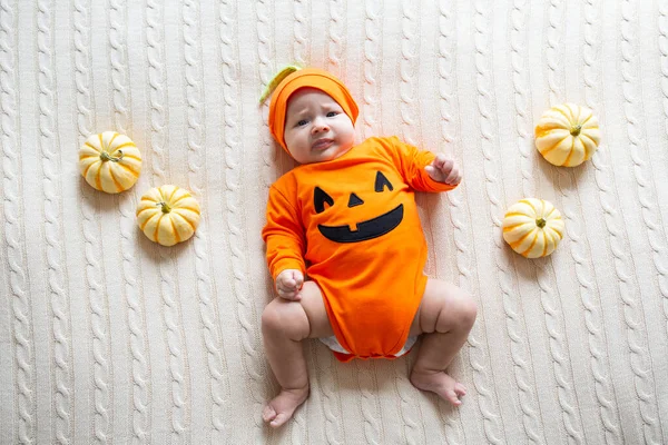 Wysoki kąt widzenia dziecka w kostiumie dyni. Happy Kid dwa miesiące w pomarańczowym kostiumie Halloween na łóżku — Zdjęcie stockowe