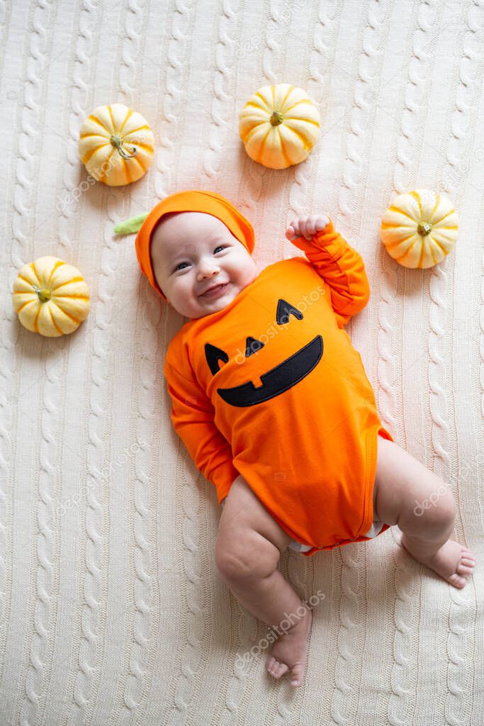 High Angle View Of Baby In Pumpkin Costume. Happy Kid two months old in orange Halloween costume on bed