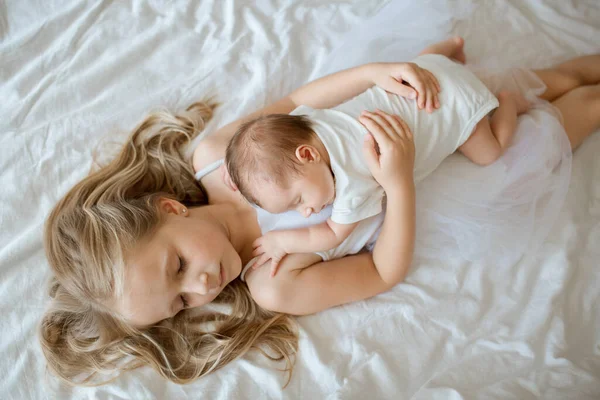 Kleine zus en haar pasgeboren broer. Een peuter die nieuwe broers en zussen ontmoet. Schattig meisje en pasgeboren baby jongen ontspannen in een slaapkamer. Gezin met twee kinderen thuis. Liefde, vertrouwen en tederheid — Stockfoto