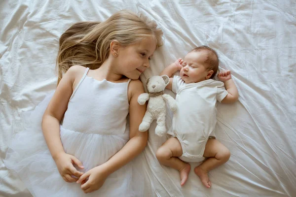 Little sister and her newborn brother. Toddler kid meeting new sibling. Cute girl and new born baby boy relax in a home bedroom. Family with two children at home. Love, trust and tenderness concept — Stock Photo, Image