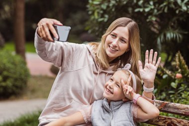 Karantinaya alınıyor. Anne ve kızı görüntülü konuşmada arkadaşlarına sesleniyor. Coronavirus covid-19 salgını sırasında sosyal mesafeler. Parkta yürüyen mutlu insanlar. Yüksek kalite fotoğraf