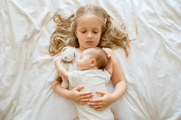 Little sister and her newborn brother. Toddler kid meeting new sibling. Cute girl and new born baby boy relax in a home bedroom. Family with two children at home. Love, trust and tenderness concept — Stock Photo, Image