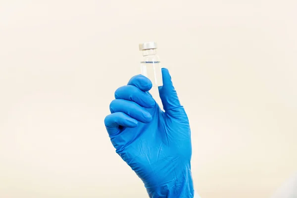 Doctor or nurse holding hands flu vaccine on beige background, measles injection syringe for baby, man, woman vaccination, medicine and drug concept. Vaccination against Coronavirus covid-19 pandemic . High quality photo
