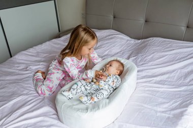Küçük kız kardeşi ve küçük erkek kardeşi. Küçük çocuk yeni kardeşiyle oynuyor. Kız ve bebek 2-3 aylıkken bir yatak odasında dinleniyorlar. Evde iki çocuklu bir aile. Aşk, güven ve şefkat kavramı. Yüksek kalite fotoğraf