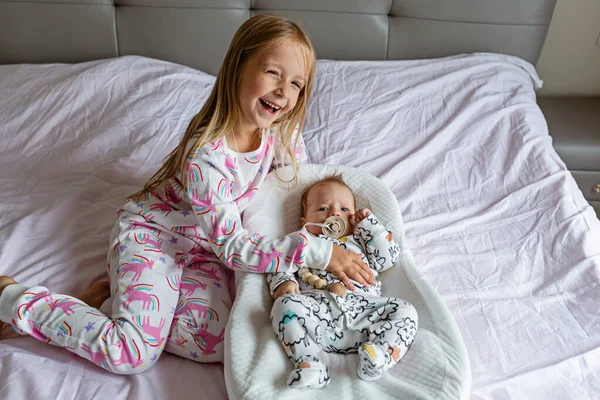Little sister and her baby brother. Toddler kid playing with new sibling. Girl and baby 2-3 months old relax in a home bedroom. Family with two children at home. Love, trust and tenderness concept. High quality photo