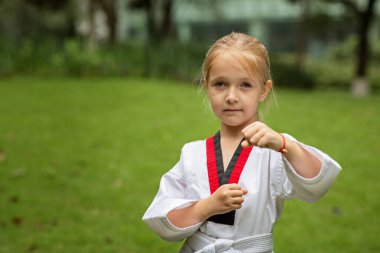Beyaz kuşaklı, altı yaşında beyaz kemerli beyaz bir kız Coronavirus covid-19 tecridi sırasında tek başına parkta tekvando yapıyor. Kişisel izolasyon ve sosyal uzaklık. Yüksek kalite fotoğraf
