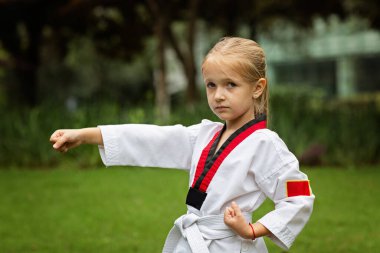 Beyaz kuşaklı, altı yaşında beyaz kemerli beyaz bir kız Coronavirus covid-19 tecridi sırasında tek başına parkta tekvando yapıyor. Kişisel izolasyon ve sosyal uzaklık. Yüksek kalite fotoğraf