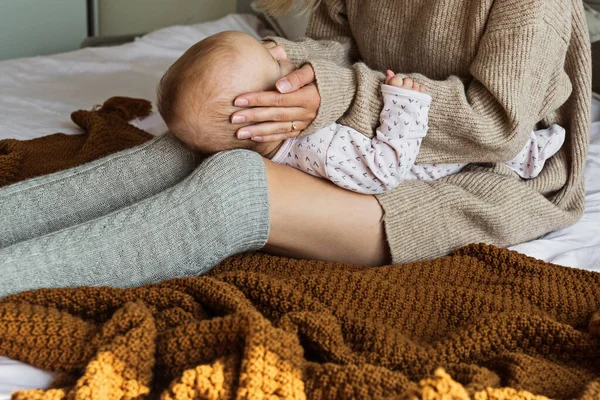 Schattig blank baby meisje liggend op gezellig bed met haar moeder gekleed in gebreide trui bruine kleur. Blijf thuis tijdens Coronavirus covid-19 quarantaine. concept van moederschap, kindertijd en gezondheidszorg — Stockfoto