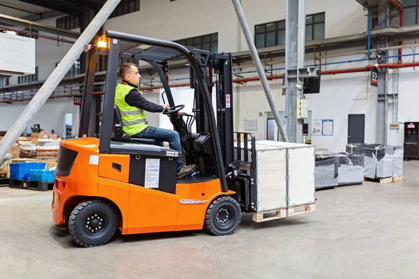 Storehouse medewerker in uniform werkt aan vorkheftruck in modern automatisch magazijn. De dozen liggen op de planken van het magazijn. Opslag, machineconcept. Logistiek in stock. — Stockfoto