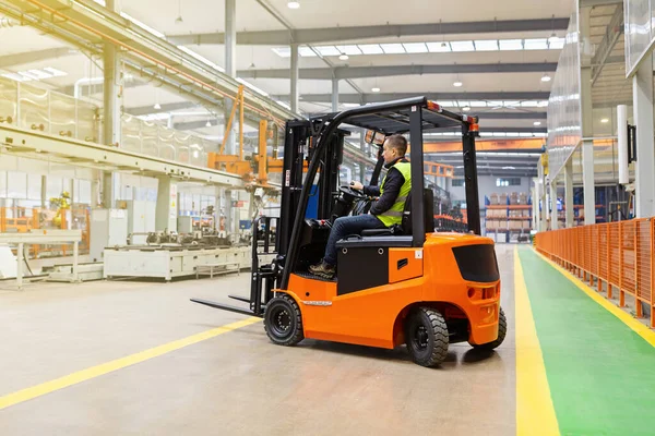 Empleado de almacén en uniforme que trabaja en carretilla elevadora en almacén automático moderno. Las cajas están en los estantes del almacén. Almacenamiento, concepto de maquinaria. Logística en stock. — Foto de Stock