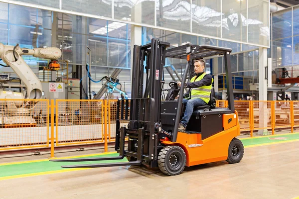 Storehouse medewerker in uniform werkt aan vorkheftruck in modern automatisch magazijn. De dozen liggen op de planken van het magazijn. Opslag, machineconcept. Logistiek in stock. — Stockfoto