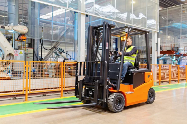 Modern otomatik depoda forklift üzerinde çalışan üniformalı bir depo çalışanı. Kutular ambarın raflarında. Depo, makine konsepti. Stokta lojistik.