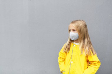 Koronavirüs salgını sırasında sarı yağmurluk ve yüz maskesi takan 7 yaşında beyaz bir kız. Yılın renkleri 2021 Nihai gri ve aydınlatıcı