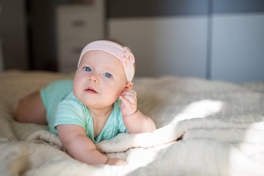 Beyaz, sarışın bir bebek. Altı aylık. Evdeki örgü battaniyenin üzerinde yatıyor. Şirin yeşil elbiseli çocuk. 