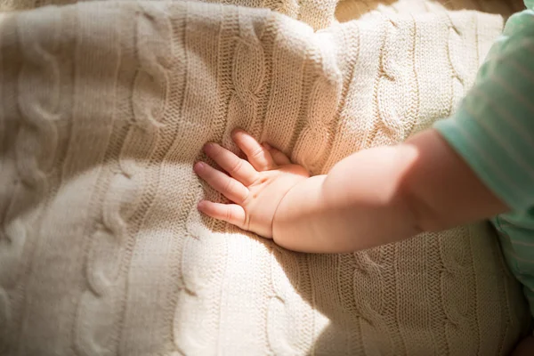 Hand van de baby zes maanden oud liggend op gezellige gebreide deken thuis. Kind draagt schattige groene kleding — Stockfoto