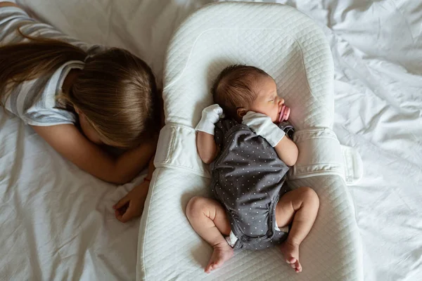 Kleine zus en haar pasgeboren broer. Een peuter die nieuwe broers en zussen ontmoet. Schattig meisje en pasgeboren baby jongen ontspannen in een slaapkamer. Gezin met twee kinderen thuis. Liefde, vertrouwen en tederheid — Stockfoto