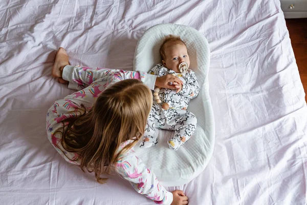 Kleine zus en haar broertje. Een peuter die speelt met een nieuw broertje of zusje. Meisje en baby 2-3 maanden oud ontspannen in een slaapkamer. Gezin met twee kinderen thuis. Liefde, vertrouwen en tederheid — Stockfoto