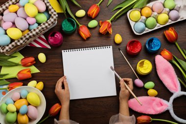 Renkli paskalya yumurtaları, ahşap arka planda pastel renkler. Elinde boya fırçası tutan bir çocuk. Düz konum, üst görünüm, model, genel görünüm, şablon