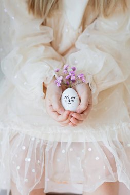 Çocuk el ele tutuşuyor. Çekilmiş yüzlü ve çiçekli mor çelenkli Paskalya yumurtaları.