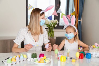 Tavşan kulağı takan, tek kullanımlık tıbbi maske takan ve Coronavirus covid-19 salgını sırasında evde paskalya yumurtası boyayan güzel bir kız.. 