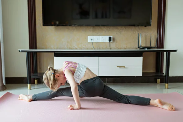 Cute little girl in sportswear doing fitness exercises at home. Distant training with personal trainer, social distance or self-isolation, online education concept