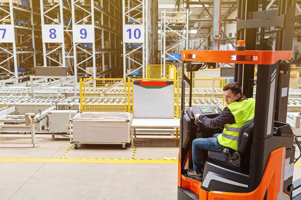 Modern otomatik depoda forklift üzerinde çalışan üniformalı bir depo çalışanı. Kutular ambarın raflarında. Depo, makine konsepti. Stokta lojistik.