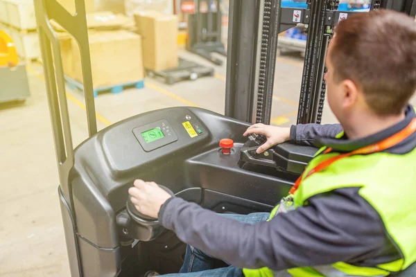 Storehouse employee in uniform working on forklift in modern automatic warehouse. Boxes are on the shelves of the warehouse. Warehousing, machinery concept. Logistics in stock.