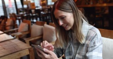 Kafede cep telefonu kullanan, sarı saçlı, beyaz, genç bir iş kadını. Ağır çekim. Teknoloji kullanan üniversite öğrencisi, çevrimiçi eğitim, serbest çalışma 