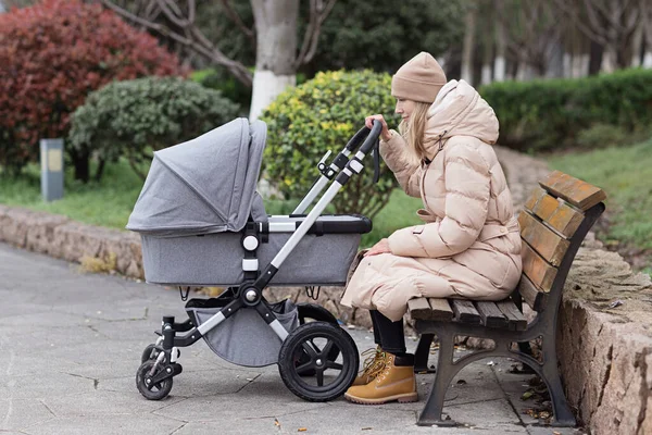 Park 'ta bebek arabasıyla gezen mutlu anne. Anneliğin neşesi. Sonbaharda kalın giysiler giyen zarif beyaz bir kadın..