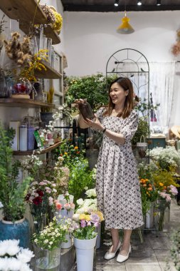 Başlangıçta başarılı küçük işletme girişimcisi çiçekçi dükkanında elinde çiçeklerle duran genç Asyalı kadın.
