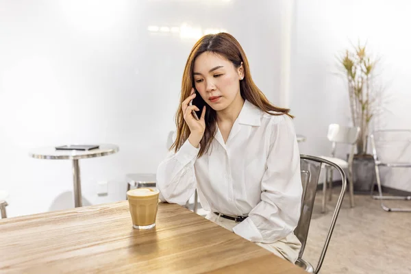 Smiling Asian Woman Talking On Cellphone In Cafe, Managing Her Business Schedule, Planning Meetings, Talking With Client or friends, Sitting At Table In modern Cafeteria