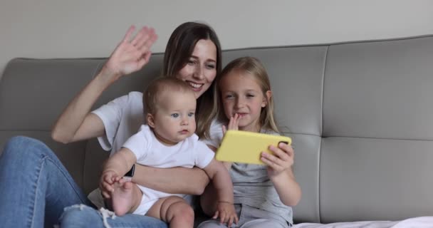 Boldog kaukázusi anya és a gyerekek van online video hívás apával vagy nagymamával a mobiltelefon, amikor feküdt az ágyon otthonos hálószobában otthon. Lassú mozgás. — Stock videók