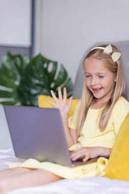 Koronavirüs salgını karantinası sırasında evde oturan ve dizüstü bilgisayar kullanan sarı renkli şık sarı saçlı, sevimli beyaz bir kız. Covid-19 sırasında evde kal.