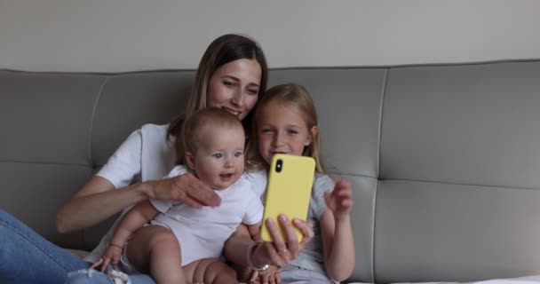 Bonne mère caucasienne et les enfants ont un appel vidéo en ligne avec le père ou la grand-mère via téléphone mobile lorsqu'ils sont couchés sur le lit dans une chambre confortable à la maison. Mouvement lent — Video