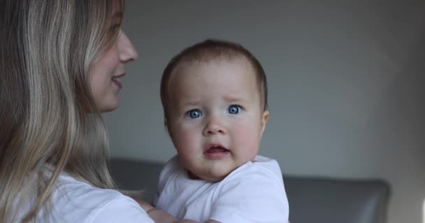 Ung kaukasisk mamma och hennes dotter kramas och leker hemma i sovrummet. Liten unge sju månader gammal tillbringa tid tillsammans med mamma armar hemma nära fönstret, slow motion. — Stockvideo