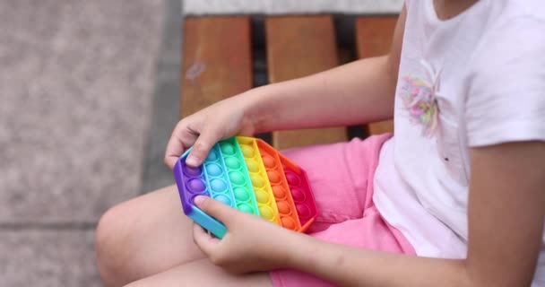 Kind spelen met regenboog pop it fidget speelgoed buiten. Push bubble zintuiglijk speelgoed - wasbaar en herbruikbaar silicium stress relief speelgoed. klein meisje speelt met anti stress eenvoudige kuiltje speelgoed. — Stockvideo