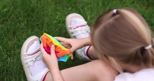 Barn leker med regnbåge pop det fidget leksak utomhus. Tryck bubbla sensorisk leksak - tvättbar och återanvändbar kisel stress leksak. Liten flicka leker med anti stress enkel dimple leksak. — Stockvideo