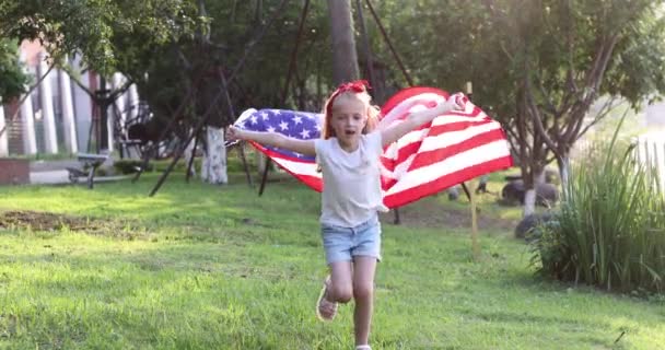 4k. Niño ondeando bandera nacional de EE.UU. al aire libre. Linda niña de siete años con cabello rubio en ropa casual corriendo en el parque al atardecer con bandera estadounidense. Feliz día de independencia 4 de julio. Despacio. — Vídeos de Stock