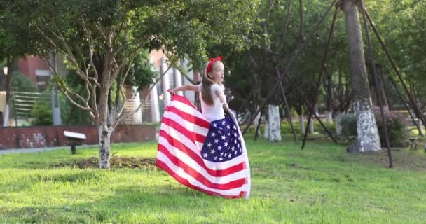 4k. Kölyök lengeti a nemzeti amerikai zászlót a szabadban. Aranyos kislány hét éves szőke hajjal alkalmi ruhában, parkol a naplementében amerikai zászlóval. Boldog függetlenség napját július 4-én. Lassú. — Stock videók