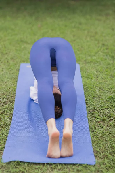 Portret van een gelukkige jonge blanke vrouw die yoga beoefent in de open lucht, vroeg in de ochtend. mooi meisje oefenen asana op blauwe yoga mat op groen gras in park in de zomer — Stockfoto