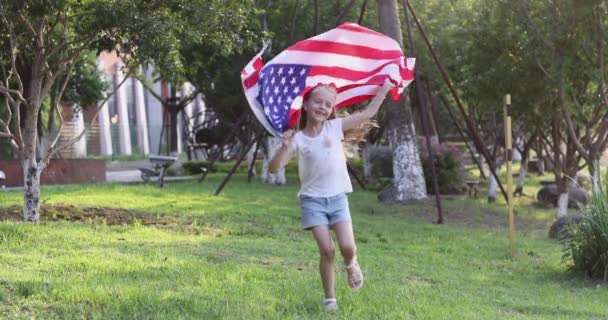 4k. Niño ondeando bandera nacional de EE.UU. al aire libre. Linda niña de siete años con cabello rubio en ropa casual corriendo en el parque al atardecer con bandera estadounidense. Feliz día de independencia 4 de julio. Despacio. — Vídeo de stock