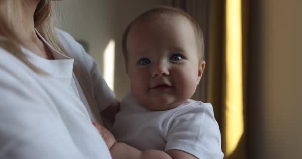 Ung kaukasisk mamma och hennes dotter kramas och leker hemma i sovrummet. Liten unge sju månader gammal tillbringa tid tillsammans med mamma armar hemma nära fönstret, slow motion. — Stockvideo