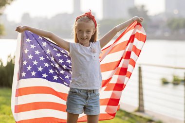 Vatansever bayram. Mutlu aile, gün batımında Amerikan bayrağı taşıyan anne ve kız. ABD 4 Temmuz 'da bağımsızlığını kutladı.