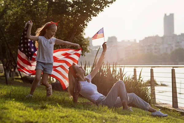 Vatansever bayram. Mutlu aile, gün batımında Amerikan bayrağı taşıyan anne ve kız. ABD 4 Temmuz 'da bağımsızlığını kutladı.