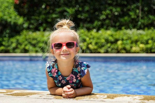 Menina branca pequena feliz com óculos de sol sorrindo alegremente e desfrutando de férias de verão tempo na piscina no hotel resort. Criança com cabelo loiro vestindo roupa de banho durante as férias de verão — Fotografia de Stock