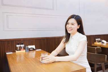 Geleneksel beyaz elbiseli güzel Asyalı kadın Cheongsam Japon restoranında ya da kafeteryasında oturmuş yemek siparişini bekliyor. Mutlu insan Çin Yeni Yılı kutluyor