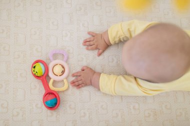 Beyaz, sarışın bir bebek. Beş aylık. Evde yatakta yatıyor. Sevimli giyinen, modaya uygun renkler giyen çocuk: nihai gri ve aydınlatıcı. Oyuncaklarla oynayan bebek