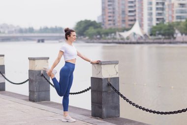 Şehirde yaz sabahı koşucu dışarıda kaslarını esnetiyor. Koşan atlet kadın spor yapıyor. Sağlıklı genç beyaz kadın egzersizden önce dışarıda ısınıyor..